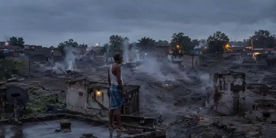बारिश के बाद ज़मीन की दरारों से उठती भाप और पीछे बस्ती के टूटे हुए मकान