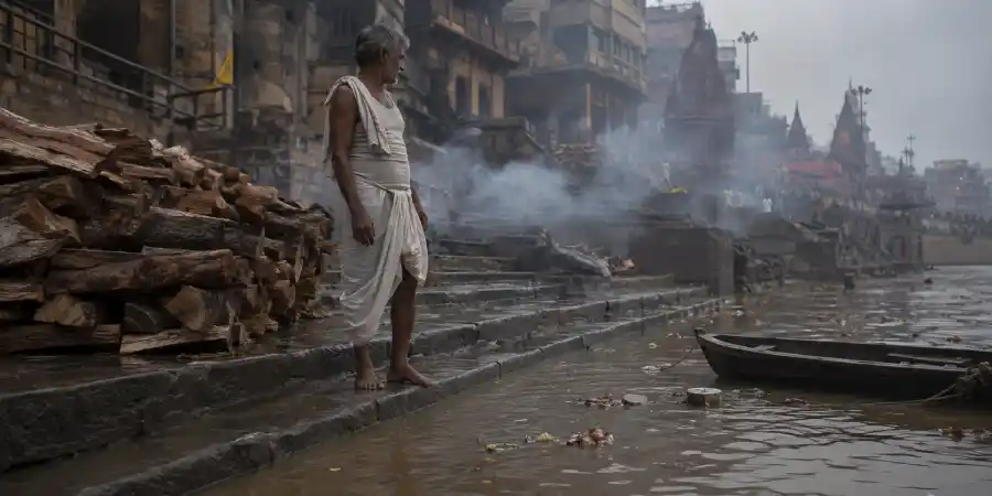 बाढ़ में डूबी घाट की सीढ़ियाँ, ऊपर बचे चबूतरे और उनसे उठता धुआँ