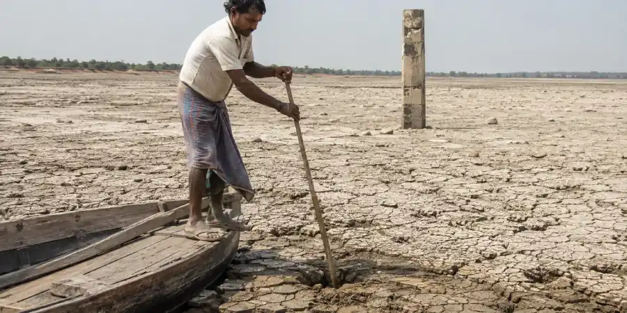 उतरी हुई झील के किनारे सूखी दरारों वाली मिट्टी और उसमें खड़ा नापने का पुराना कंक्रीट का खंभा